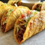 Close-up of crispy Air Fryer Tacos Extravaganza filled with seasoned meat, lettuce, cheese, tomatoes, and sour cream.