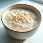 A bowl of creamy Coconut Cream Oats topped with toasted coconut flakes and a sprinkle of cinnamon.
