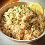 A bowl of Greek Lemon Rice garnished with fresh parsley and a lemon wedge.