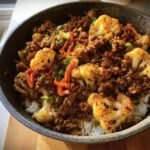 A bowl of Ground Beef Cauliflower Skillet, garnished with green onions and red bell peppers, served over rice.