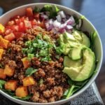 Overhead shot of a Ground Beef Protein Bowl with quinoa, avocado, tomatoes, red onion, and spinach.