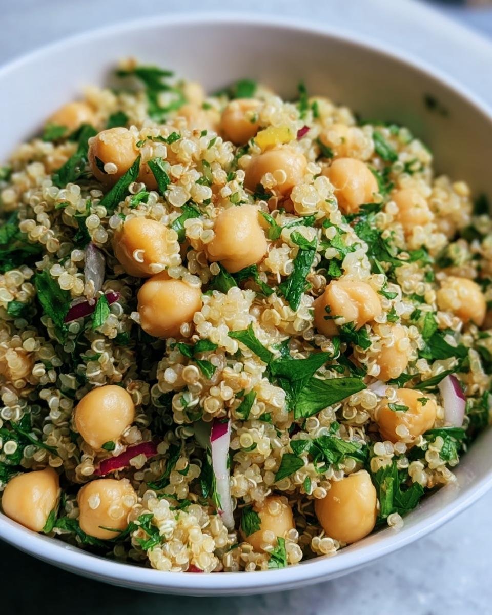 Close-up of Lemon Herb Quinoa Chickpeas in a white bowl, garnished with fresh herbs and red onions.