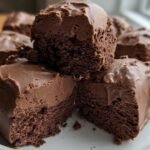Close-up of several pieces of No-Bake Cottage Brownie with chocolate frosting on a white plate.