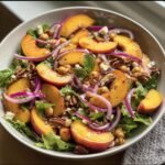 A vibrant Peach Salad with Honey Lime dressing, featuring fresh peaches, red onion, nuts, and feta cheese.