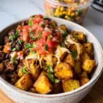 A close-up of Potato Taco Bowls in a bowl, topped with salsa, cheese, cilantro, and black beans.