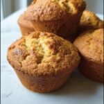 Several freshly baked Pumpkin Cottage Cheese Muffins stacked on a white surface.