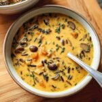 Close-up of a bowl of Pumpkin Wild Rice Soup with mushrooms and herbs, ready to eat.