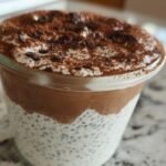 Close-up of Viral Tiramisu Chia Pudding in a glass, showing layers of chia seeds, cream, chocolate, and cocoa powder.