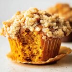 Close-up of an apple pumpkin streusel muffin with a bite taken out, showing the moist interior and crumbly topping.