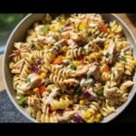 A bowl of BBQ Chicken Pasta Salad with grilled chicken, pasta, corn, and red onion.