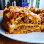 Close-up of a slice of Bundt Pan Nachos, showing layers of tortilla chips, ground beef, and melted cheese.