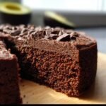 Close-up of a moist Chocolate Avocado Cake slice topped with chocolate chunks, showcasing its texture.