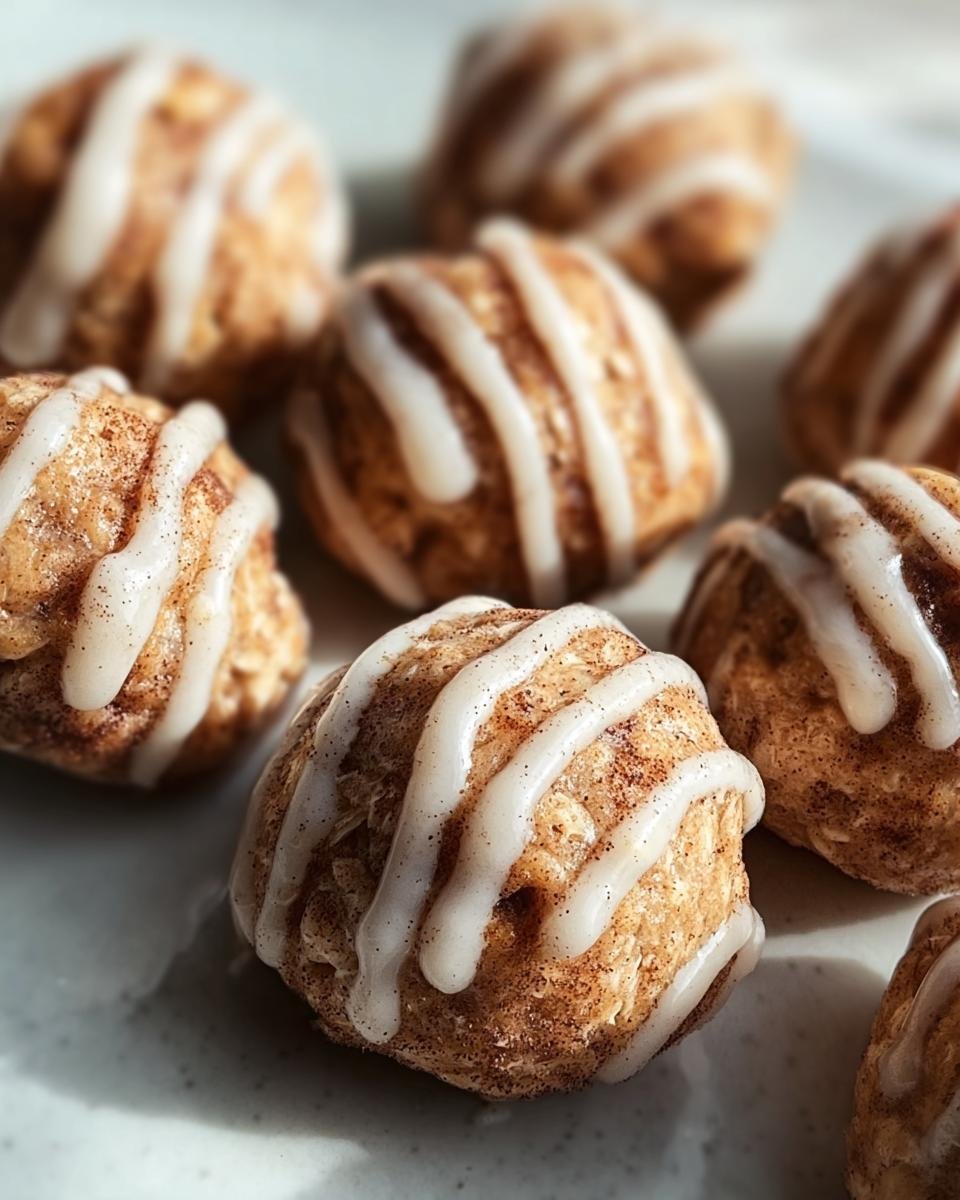 Close up of several Cinnamon Roll Protein Bites drizzled with white icing on a plate.