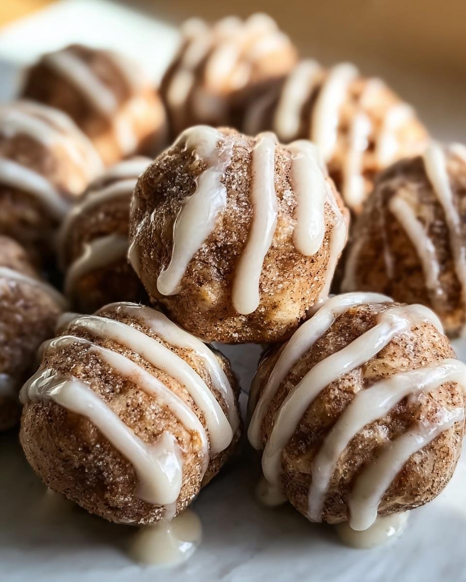 A close-up of Cinnamon Roll Protein Bites drizzled with white icing, stacked on a plate.