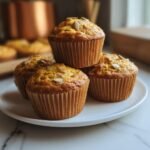 A stack of four Cottage Cheese Pumpkin Muffins on a white plate, topped with pumpkin seeds.