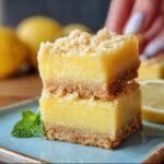 Two stacked Creamy Lemon Squares on a plate, featuring a crumbly crust, creamy lemon filling, and crumble topping.