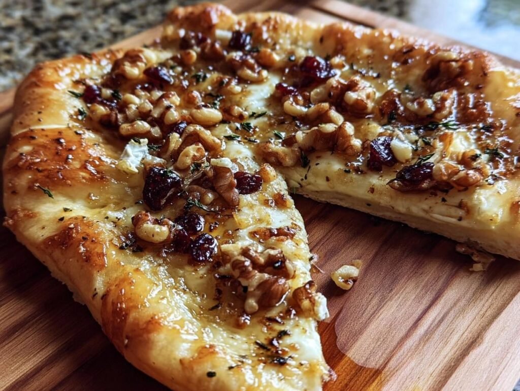 Close-up of Crispy Flatbread with Brie, topped with walnuts, cranberries, and herbs on a wooden board.