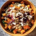 Overhead shot of a colorful Fall Harvest Salad in a wooden bowl with squash, quinoa, cranberries, and feta.