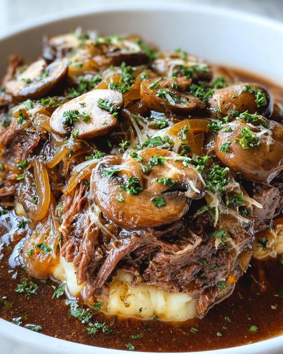 Close-up of French Onion Pot Roast with shredded beef, caramelized onions, mushrooms, and gravy over mashed potatoes.