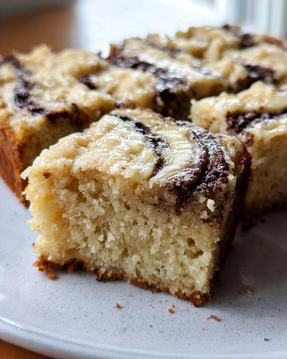 Close-up of a slice of Irresistible Banana Bars with chocolate swirl frosting on a white plate.