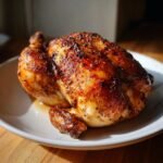 A whole roasted Melt In Your Mouth Chicken, seasoned and golden brown, served on a white plate.