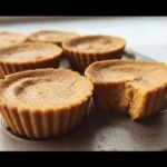 Close-up of freshly baked Mini Pumpkin Pie Cups in a muffin tin, one with a bite taken out.