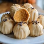A stack of Pumpkin Cheesecake Truffles, one cut in half to show the pumpkin filling, topped with chocolate chips.
