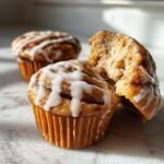 Close up of Pumpkin Cinnamon Roll Muffins with icing, one muffin torn open to show the inside.