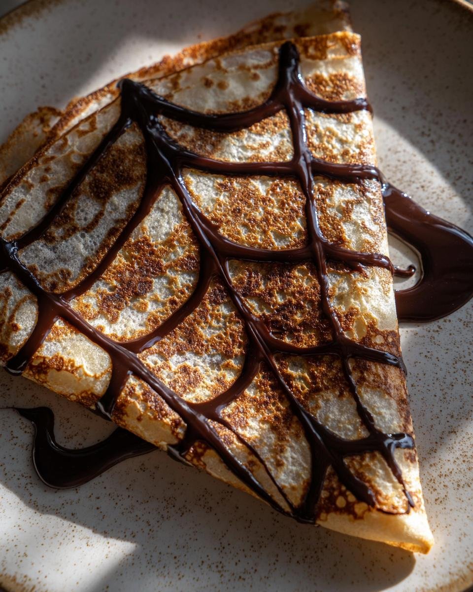 A delicious spiderweb crepes, folded and drizzled with chocolate syrup in a spiderweb pattern.