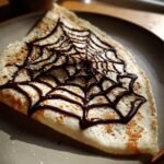 A delicious spiderweb crepes with a chocolate spiderweb design on a plate.