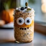 Jar of Overnight Oats with Spooky Toppings: candy eyes, pumpkin puree, blackberries, and coconut flakes.