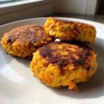 Three golden-brown SWEET POTATO & RED LENTIL PATTIES stacked on a white plate, ready to be enjoyed.