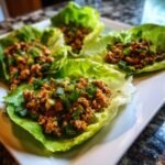 Four Turkey Lettuce Wraps (PF-Style) on a white plate, filled with seasoned ground turkey and garnished with green onions.