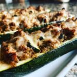 Close-up of Turkey & Quinoa Stuffed Zucchini Boats, topped with melted cheese, on a white plate.