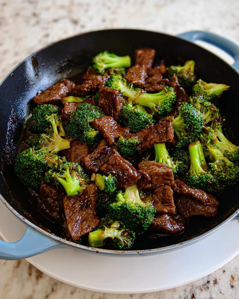Close-up of tender pieces of beef and bright green broccoli florets coated in a savory sauce, ready to serve in a blue-handled skillet.