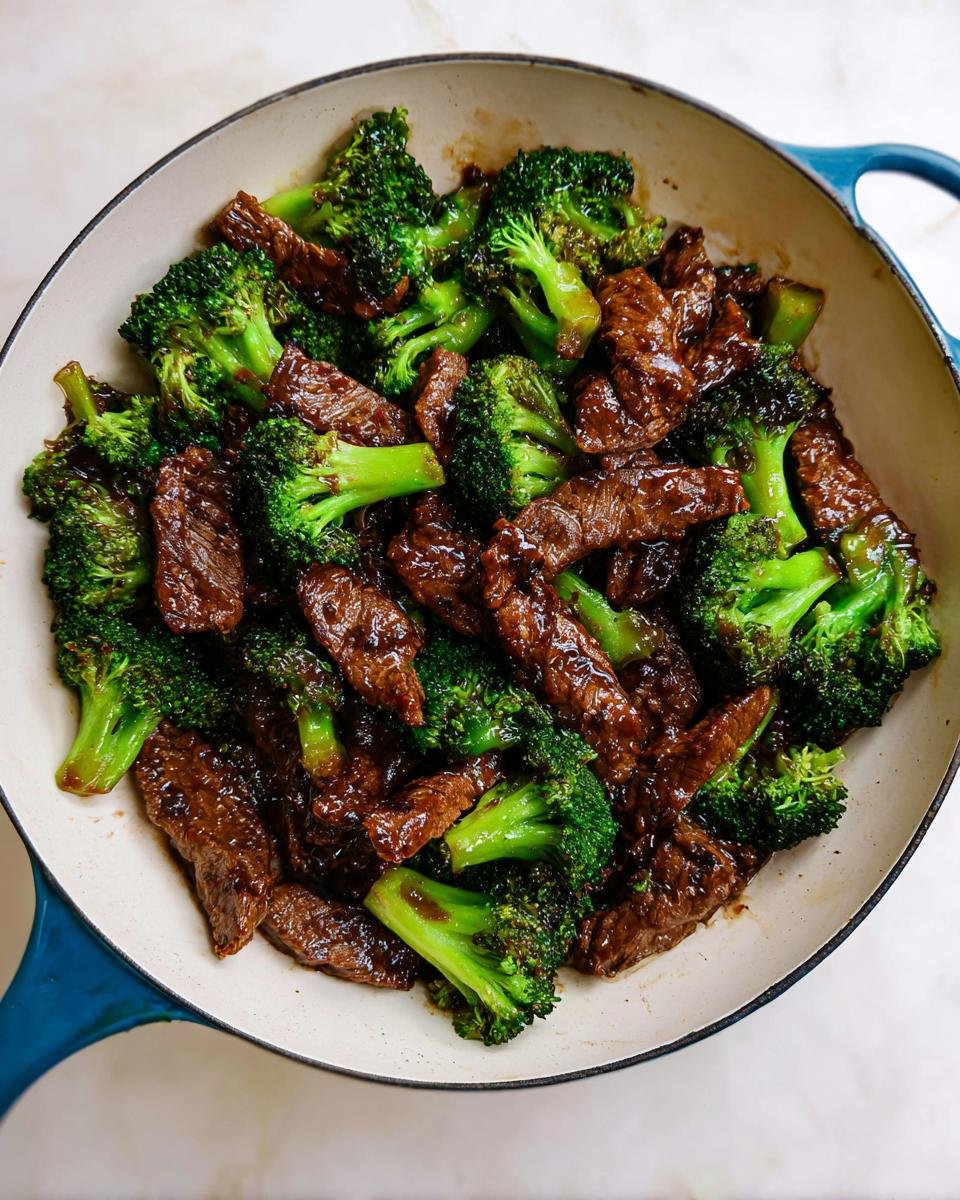 Close-up overhead shot of glossy Beef and Broccoli Stir Fry cooked in a white and blue enameled skillet.