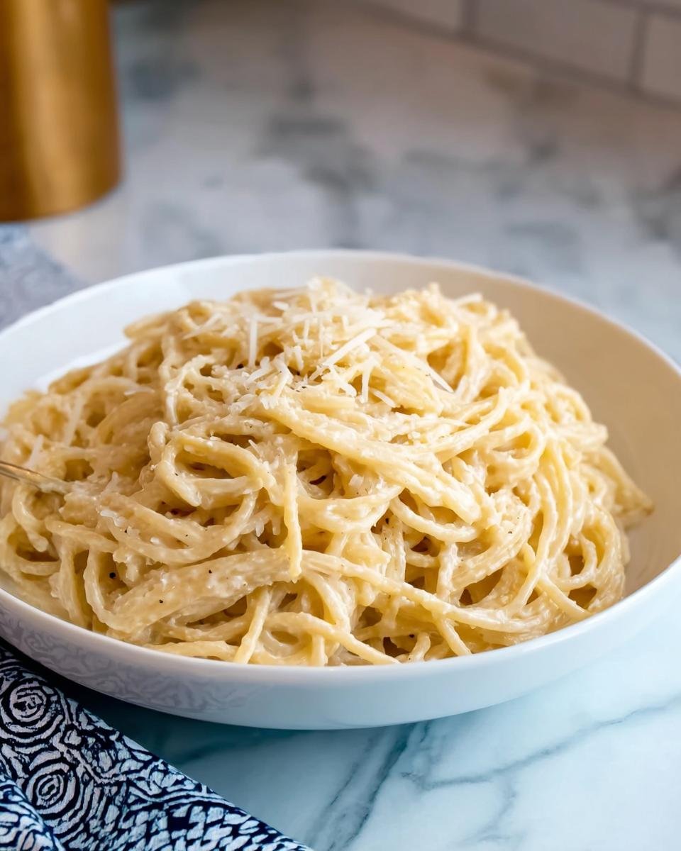 A white bowl filled with rich Creamy Garlic Pasta, topped with grated Parmesan cheese.