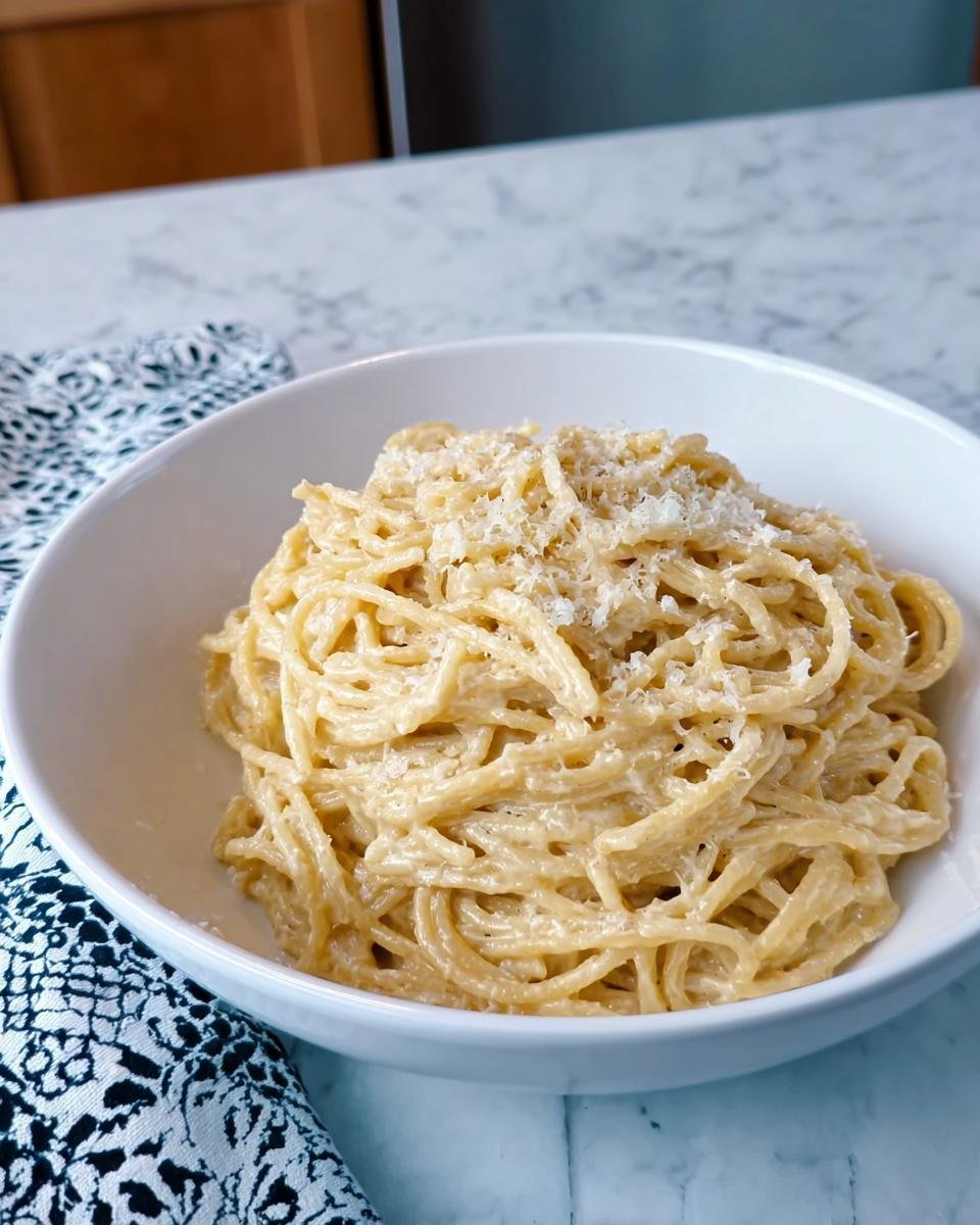 A white bowl filled with rich Creamy Garlic Pasta, topped with grated Parmesan cheese, sitting on a marble counter.