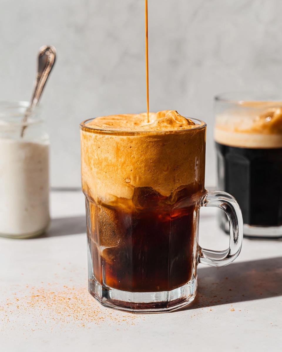 A stream of rich orange Pumpkin Cream Cold Foam is being poured onto a glass of iced coffee.