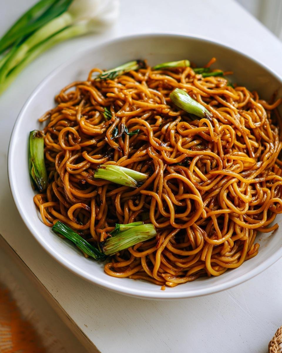 A white bowl filled with glossy, brown soy-glazed noodles topped with bright green scallions, perfect for 5-Ingredient Dinners.