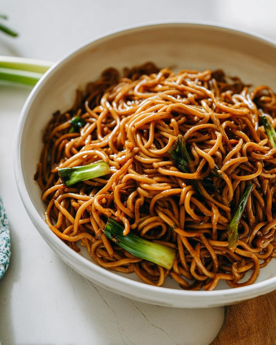 Close-up of glossy, saucy noodles garnished with bright green scallions, perfect for 5-Ingredient Dinners.