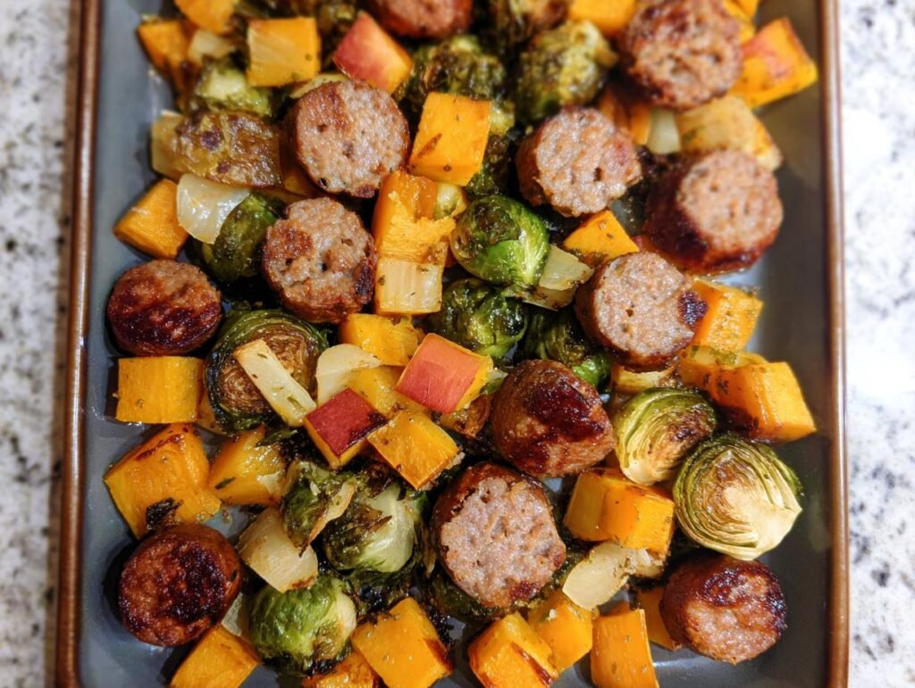 Close-up of sausage slices, roasted Brussels sprouts, and cubed butternut squash on a sheet pan, perfect for Sheet Pan Suppers.