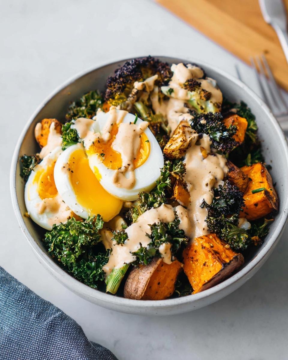 A bowl featuring a balanced meal with soft-boiled eggs, roasted sweet potatoes, kale, and creamy dressing.