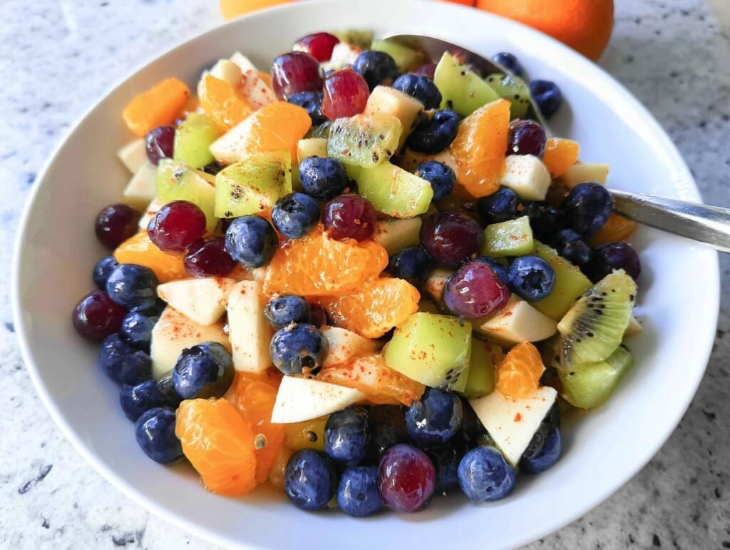 Close-up of a vibrant Love-Themed Fruit Salad featuring blueberries, oranges, kiwi, and grapes in a white bowl.