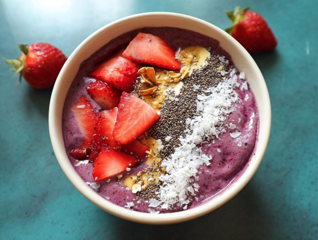 Overhead view of a vibrant Protein-Packed Smoothie Bowl topped with sliced strawberries, chia seeds, coconut flakes, and granola.
