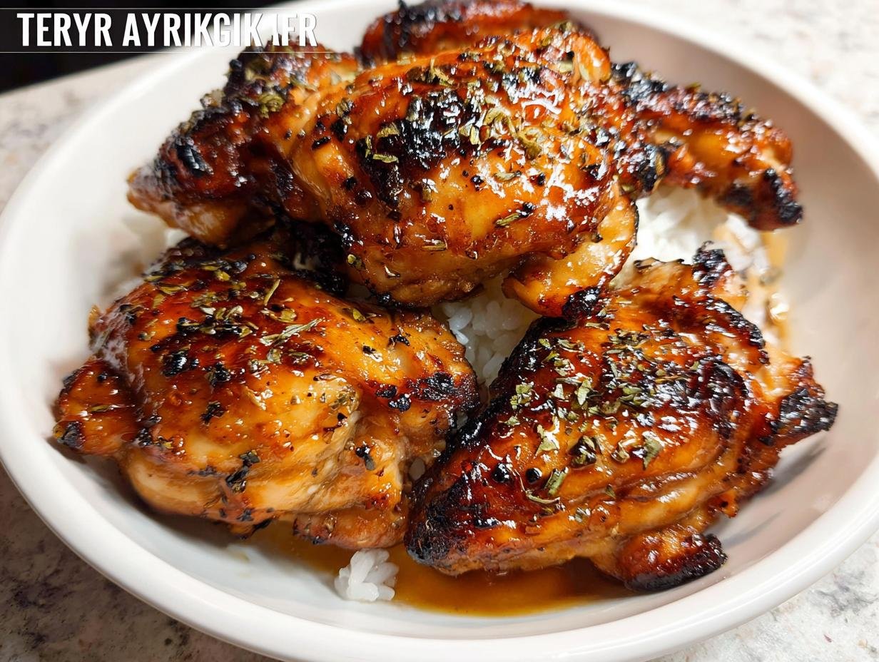 Close-up of juicy Air Fryer Teriyaki Chicken Thighs glazed with sauce and sprinkled with herbs, served over white rice.