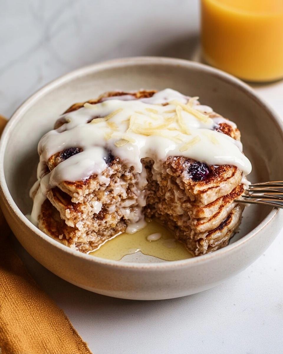 A stack of Cinnamon Roll Pancakes cut open, drizzled with white icing and topped with zest.
