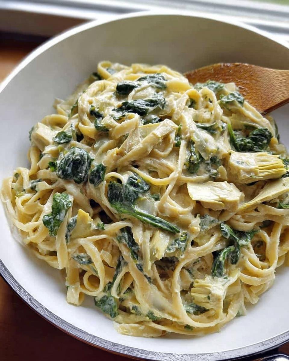 Close-up of fettuccine coated in a rich sauce with spinach and artichoke hearts, ready to eat, showcasing Creamy Spinach Artichoke Pasta.