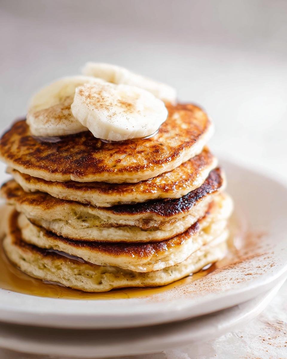 A tall stack of fluffy Protein Pancakes Fluffy topped with sliced banana and cinnamon.