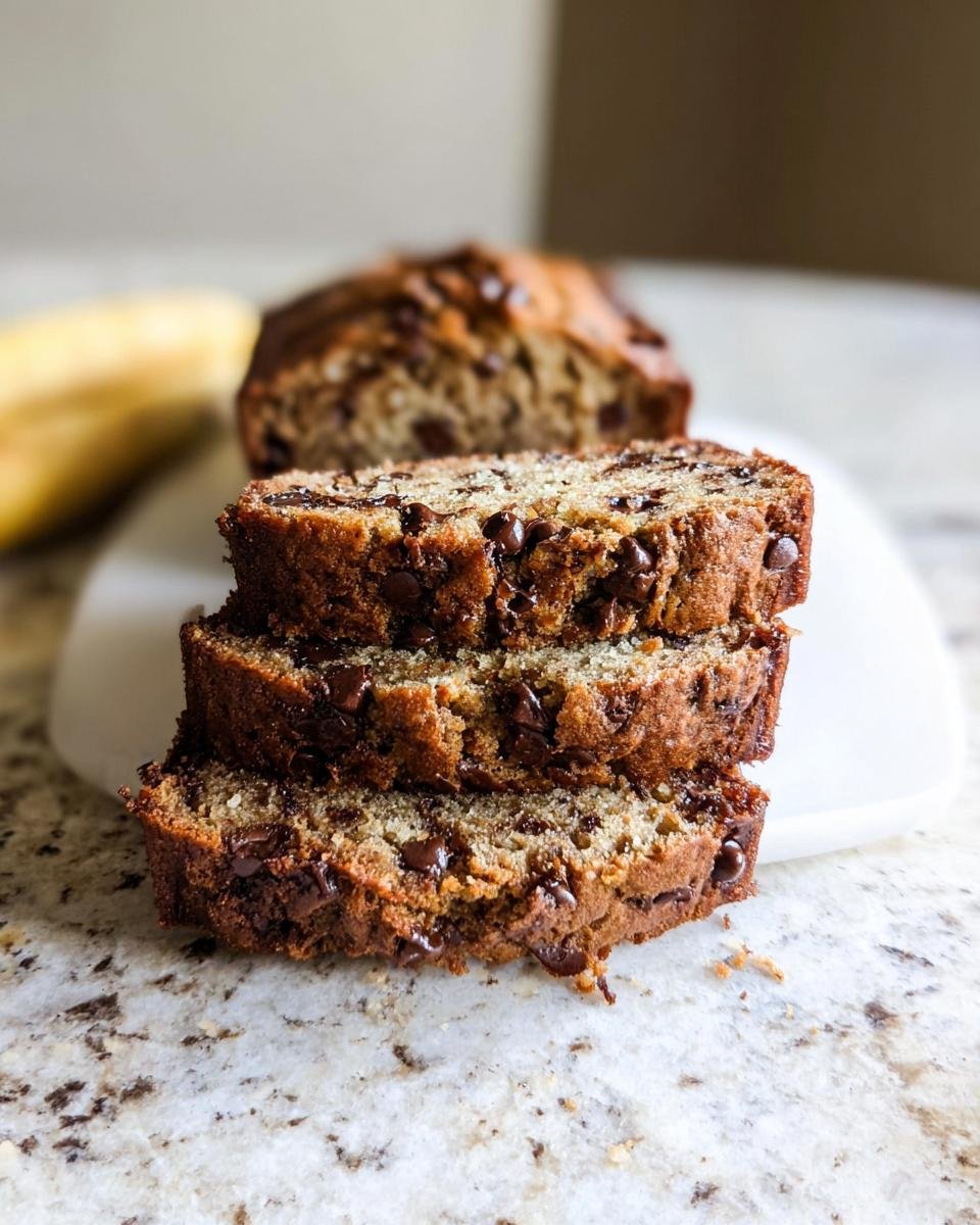 Three stacked slices of moist chocolate chip banana bread on a marble countertop.